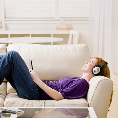Woman laying on sofa and listening to music on headphones