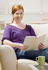 Relaxed woman sitting on sofa enjoying reading book