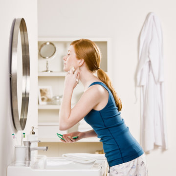 Woman in pajamas in bathroom applying blush