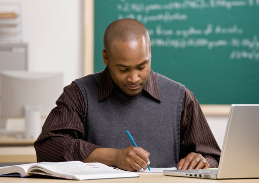 Teacher with laptop grading papers in school classroom