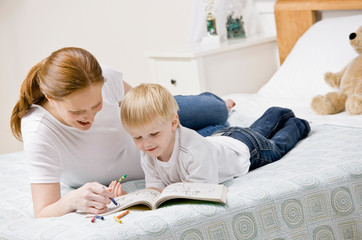 Mother coloring in coloring book with son on bed in bedroom