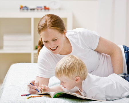 Mother coloring in coloring book with son on bed in bedroom