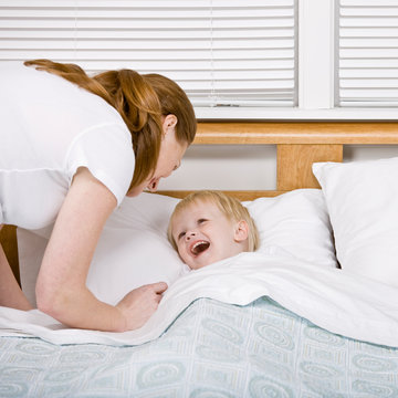 Devoted mother putting talkative son to bed at bedtime