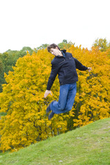 The guy cheerfully jumps against a tree with yellow leaves