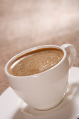 Cup of black coffee with froth on brown background, shallow DOF