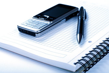 Pen, spiral notepad and mobile phone on white background