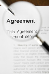 Magnifying glass over agreement paperwork and pen.