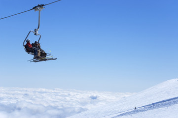 Fototapeta na wymiar Wyciąg krzesełkowy z narciarzy w ośrodku narciarskim ponad chmurami