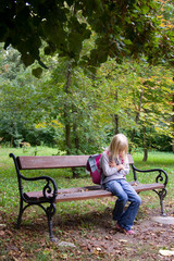 A very sad schoolgirl sitting on a bench at a park.