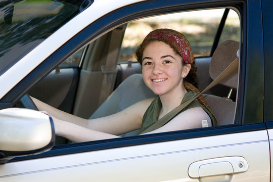 Pretty teen driver smiling behind the wheel of her new car.