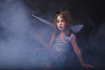 Little beautiful girl in blue dress with wings posing in  fog.