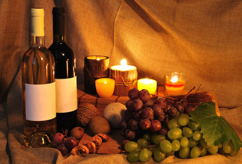 Two bottle of wine and grapes, lighted by candles