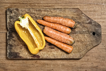 Yellow bell pepper and carrots on a wooden cutting table.