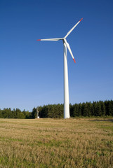 Fototapeta premium Wind turbine against blue sky with the forest in background