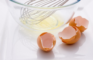 Three broken eggs and a bowl with egg white and whisk