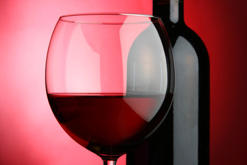 Glass and bottle of wine over red background