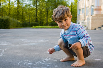 4 year old boy draws with chalk on asphalt