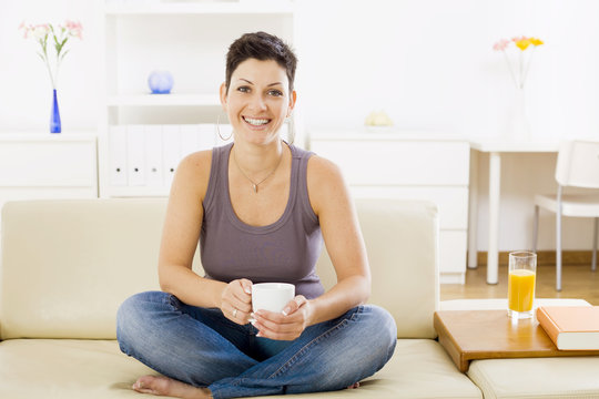 Young woman sitting on sofa at home, drinking coffee.