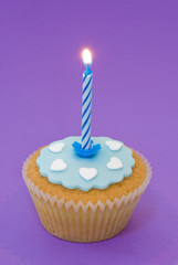 Single cupcake with blue lit candle and icing