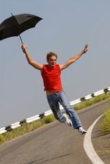 young  man jumps with  umbrella on road