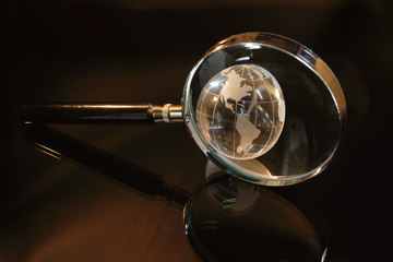 Magnifier and little glassy earth on dark background