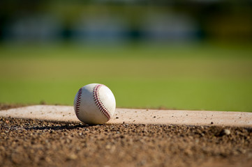 A white leather baseball lying on top of the pitcher's mound - 9891200