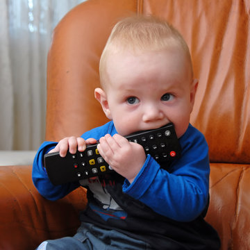 Adorable baby boy chewing the TV remote control