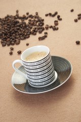 Cup of cappuccino with cinnamon and spilled out coffee beans.