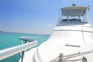 A close-up view of the front deck of a sleek white luxury yacht cruising over a crystal-clear turquoise sea under a bright blue sky. Perfect image for travel, tropical vacation, maritime lifestyle, or