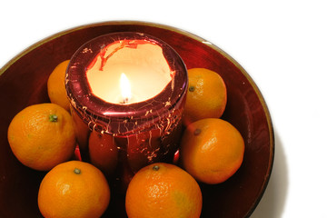 oranges set around a christmas candle in a red glass bowl
