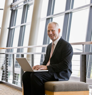 Happy businessman working on laptop in office lobby