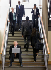 Businessman sitting and working on laptop on busy office stairs