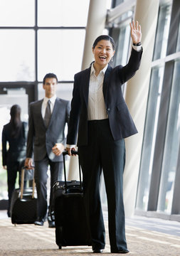 Business traveler pulling suitcase and waving to co-worker