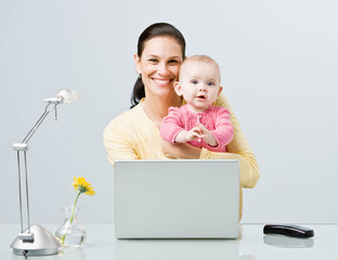 Working mother holding baby while typing on laptop at desk