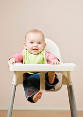 Happy, hungry baby in bib sitting in highchair