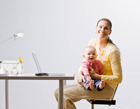 Working mother holding baby with laptop on desk