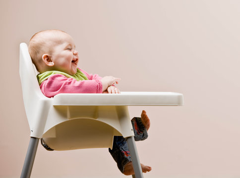 Laughing, hungry baby in bib sitting in highchair