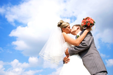 young bride and groom kissing against blue sky