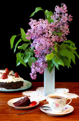 Lilacs in vase on table with dessert and tea