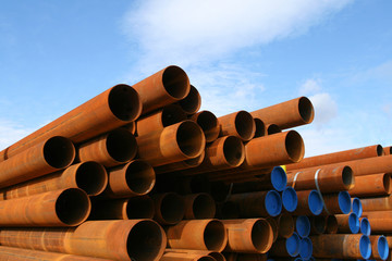 Rusty steel pipes, stacked against blue sky - 9969256