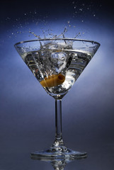 Cocktail splash with an olive on blue background