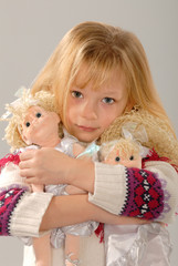 cute blonde girl with wistful expression holds dolls