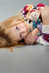 cute blond girl cuddles her doll, laying down