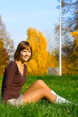 The young girl on a green grass in autumn park