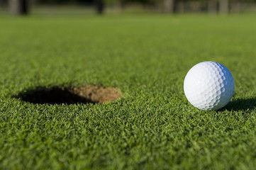 A white golf ball near the hole of a golfing green or course