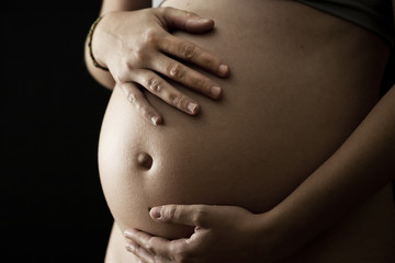 A young pregnant woman holding her abdomen on a black background