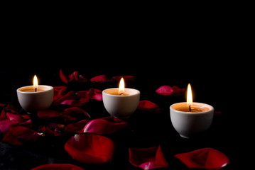 Obraz na płótnie Canvas Three Candles and red rose petals .