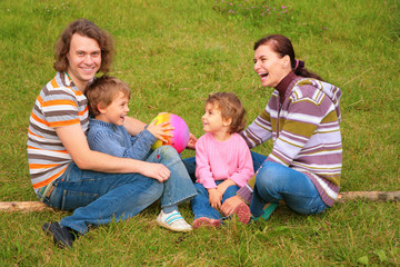 Naklejka na ściany i meble Family of four sits on grass