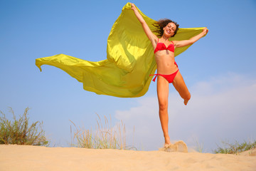 Young girl on sand with yellow fabric shawl in hands