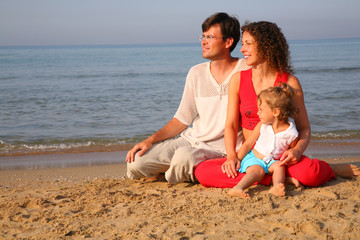 Parents with child sitting on sand on seashore